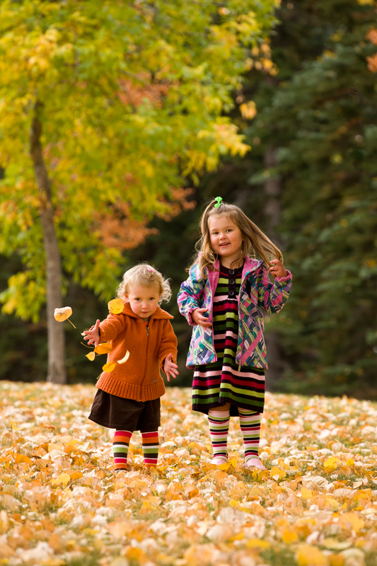 Two young girls dressed for the chill playing with fallen leaves.